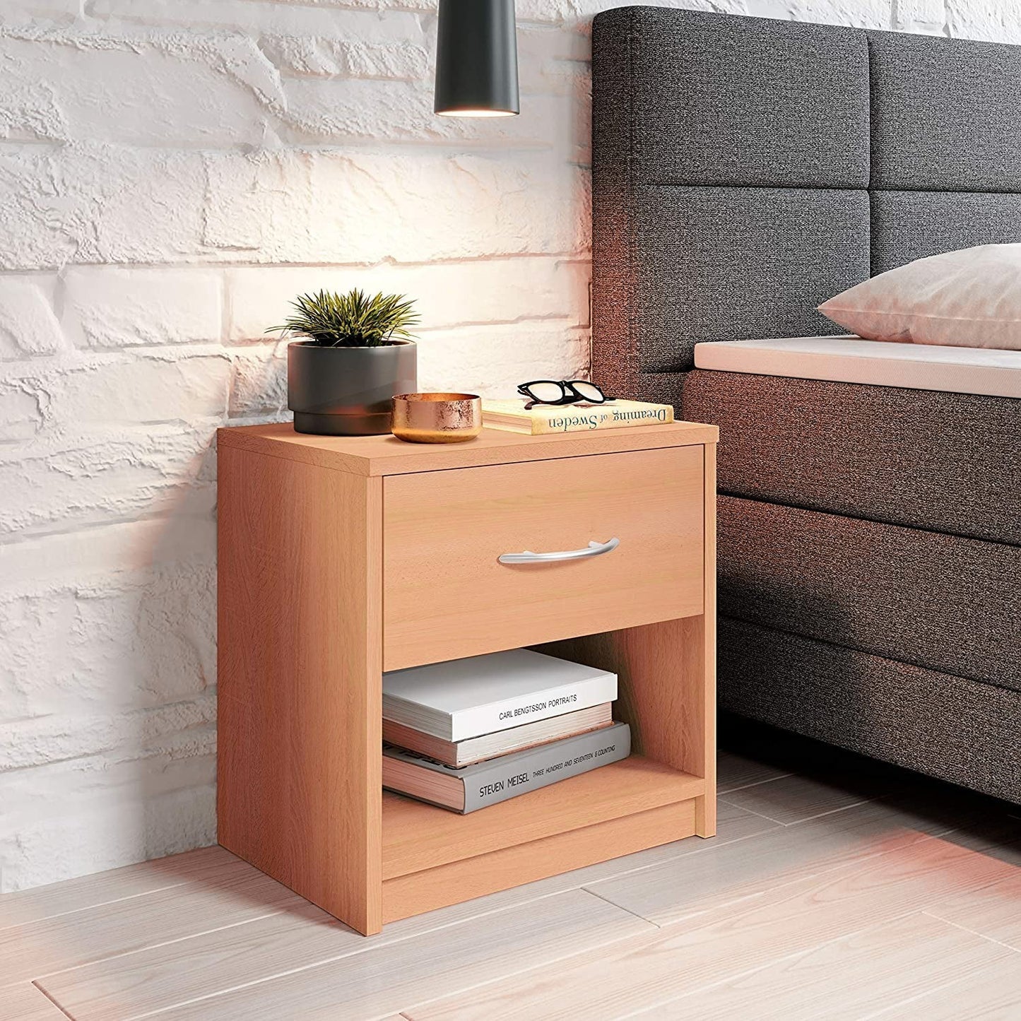 Modern Home light wood bedside table with a drawer and open shelf, placed next to a grey upholstered bed.