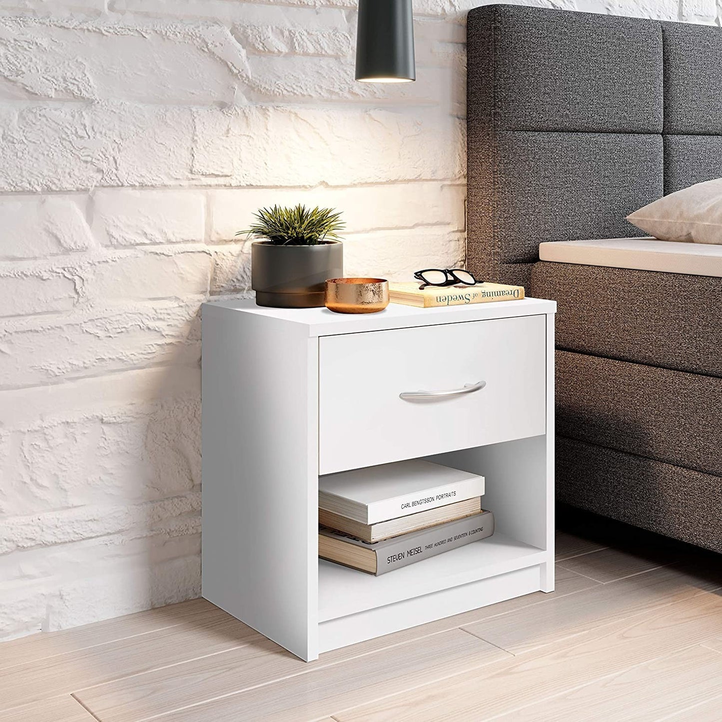 Modern Home white bedside table with a drawer and open shelf, featuring an aluminum handle next to a grey bed.