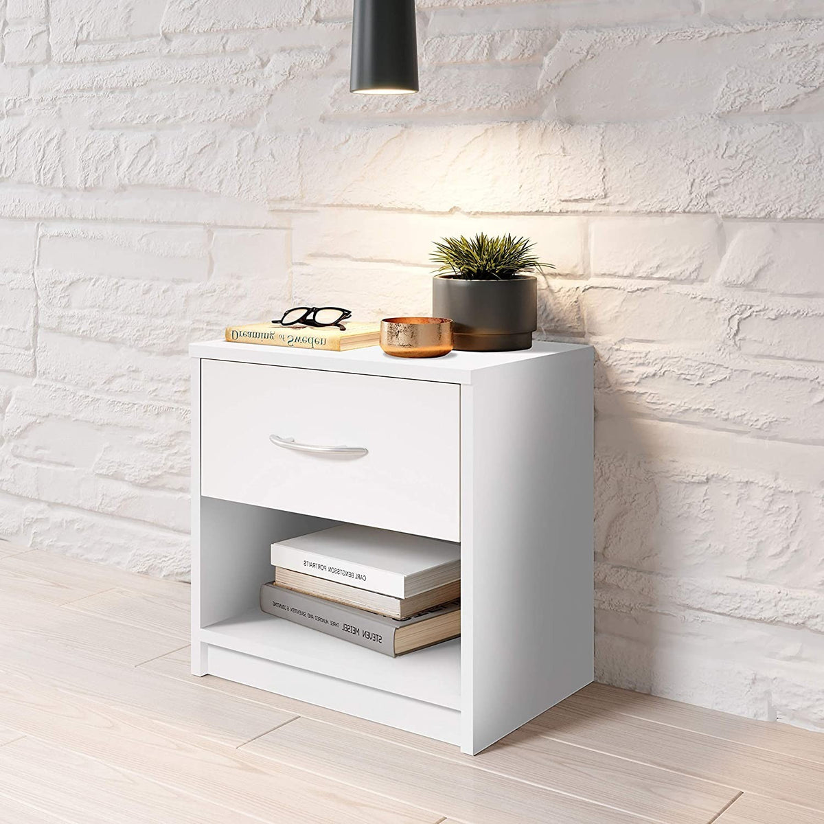 Modern Home white bedside table with a drawer, aluminum handle, and open shelf against a white brick wall.